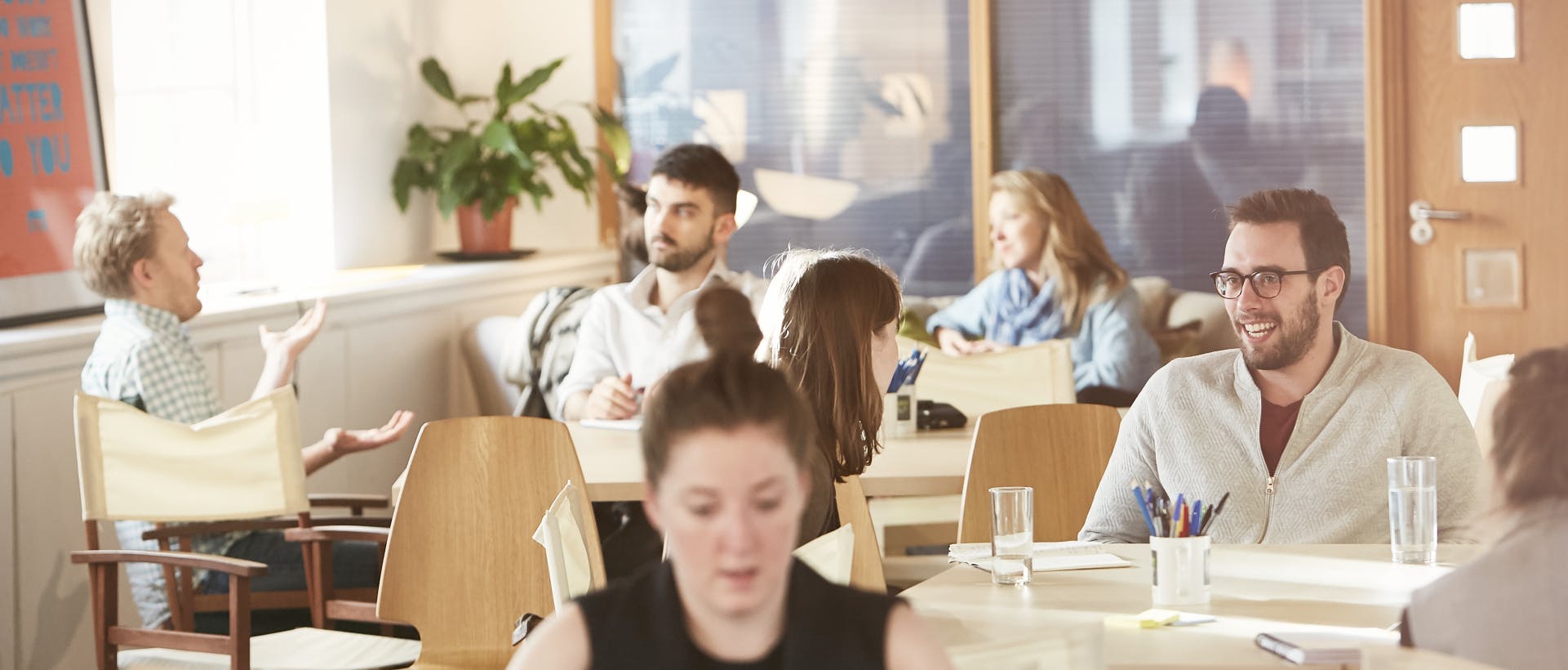 People sitting around several tables talking and smiling with water cups and notebooks in front of them