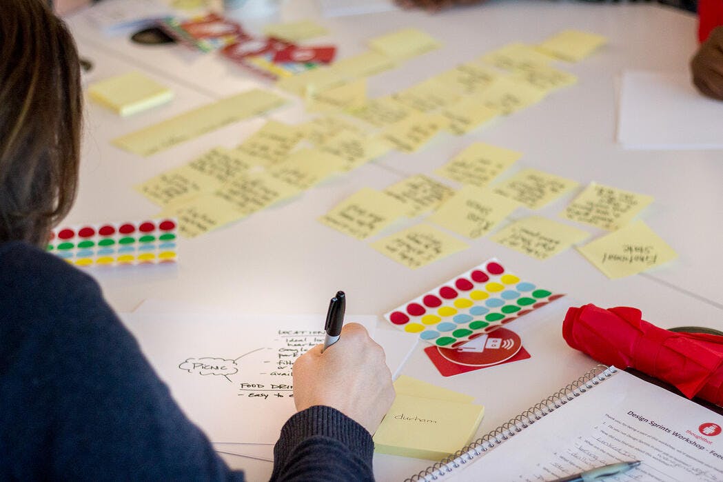 A person drawing on a piece of paper on a desk covered in sticky notes.