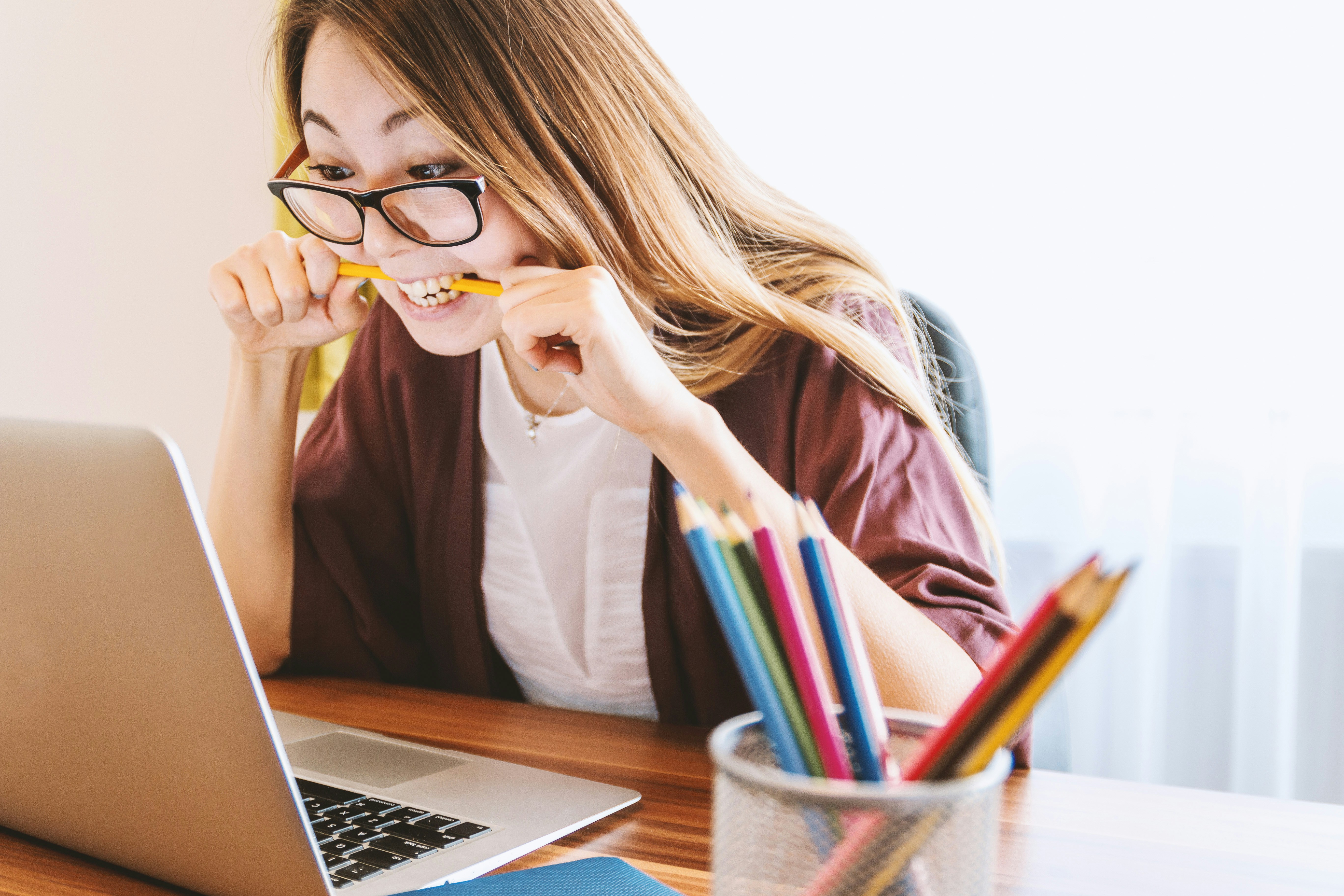 woman biting pencil while looking at computer